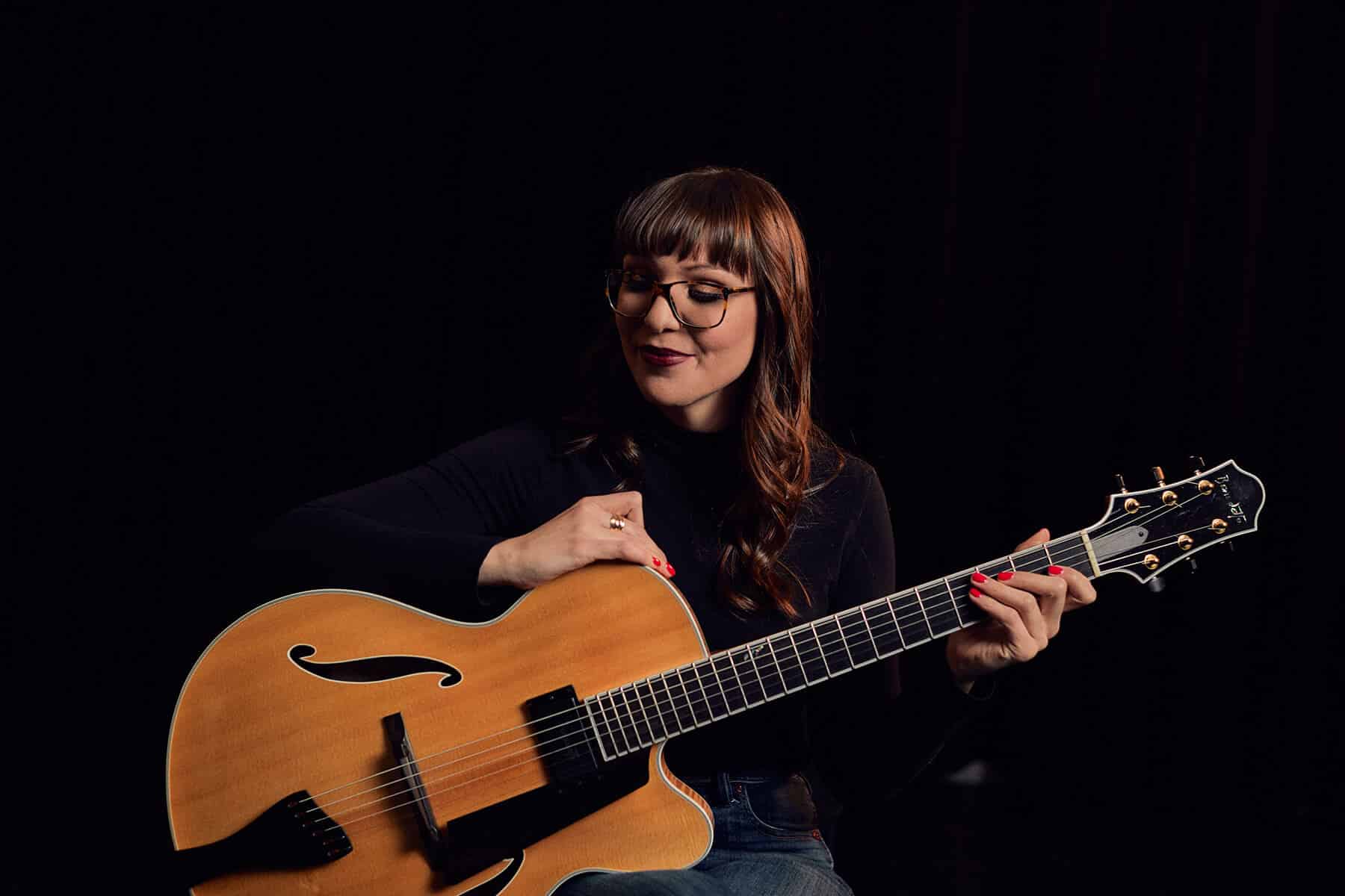 Jocelyn Gould against a black background holding her Benedetto guitar.
