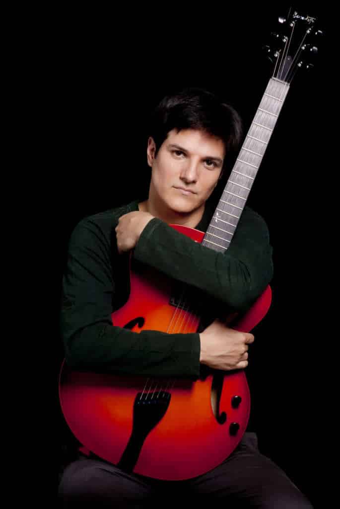 Chico holding a red Benedetto guitar.