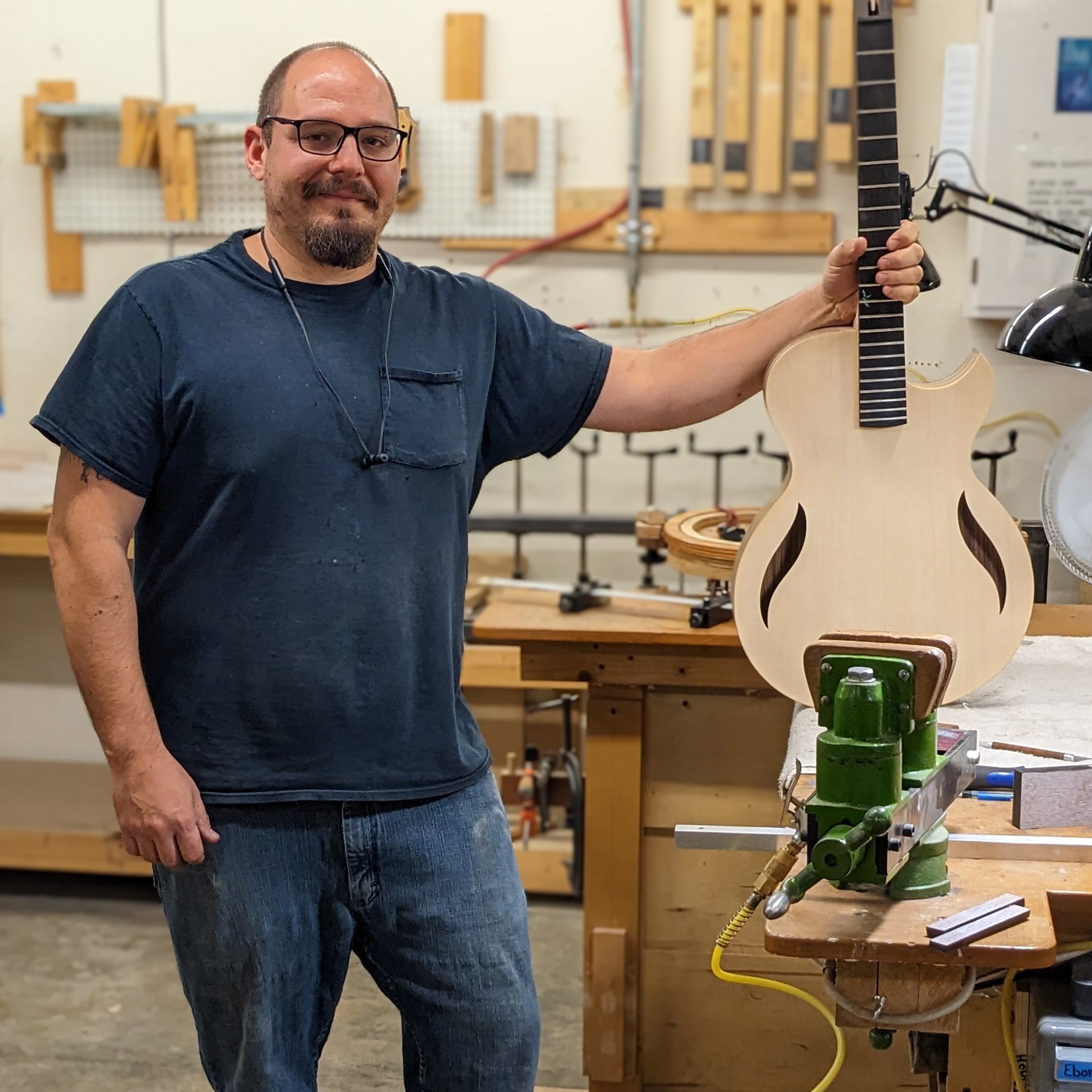 Luthier, Steve Holzknecht hold an in-progress guitar at his bench.