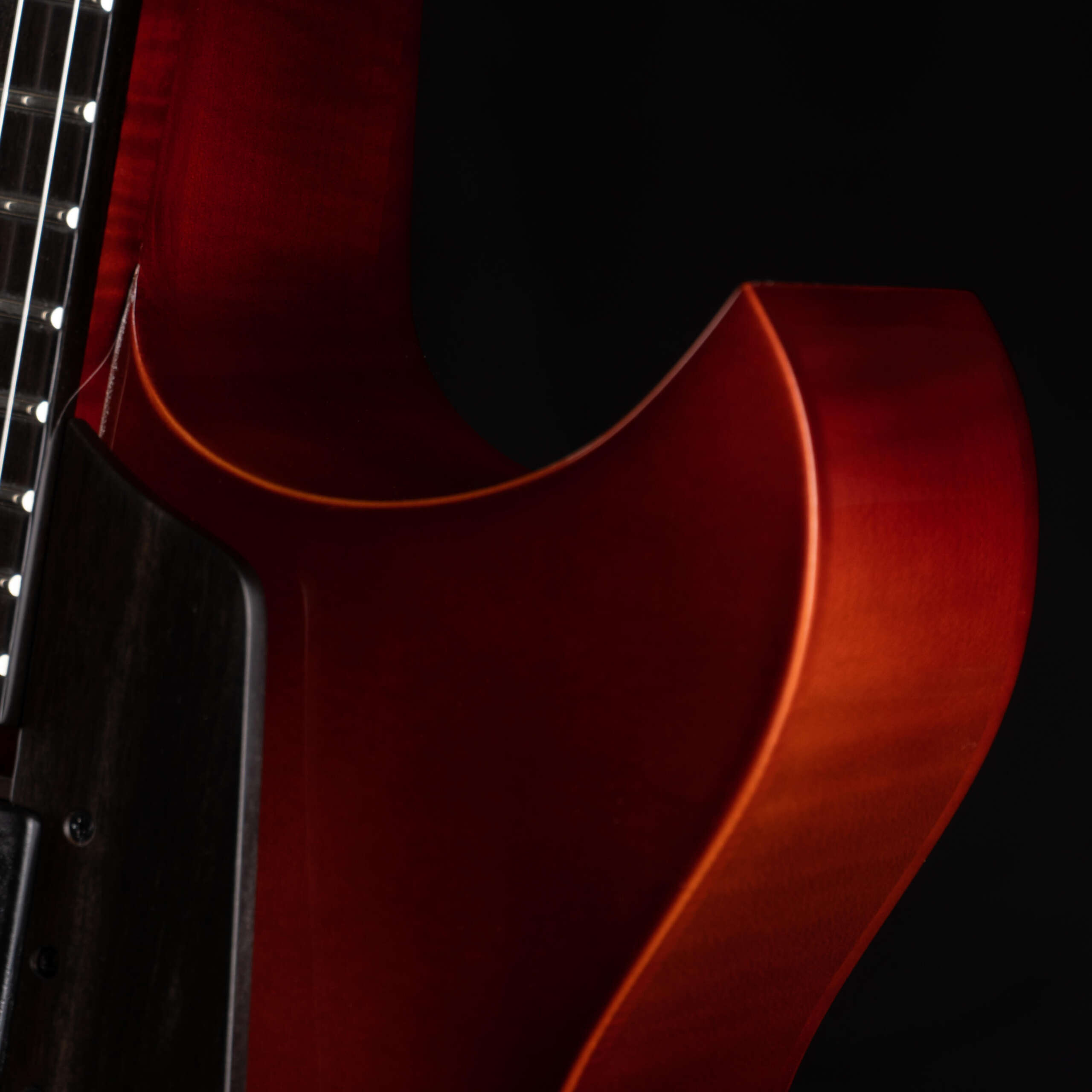 A dramatic close-up of a Benedetto archtop guitar's upper horn, displaying a vibrant sunburst finish over highly flamed tonewood back and sides, with a dark ebony fingerboard edge visible under soft studio lighting.