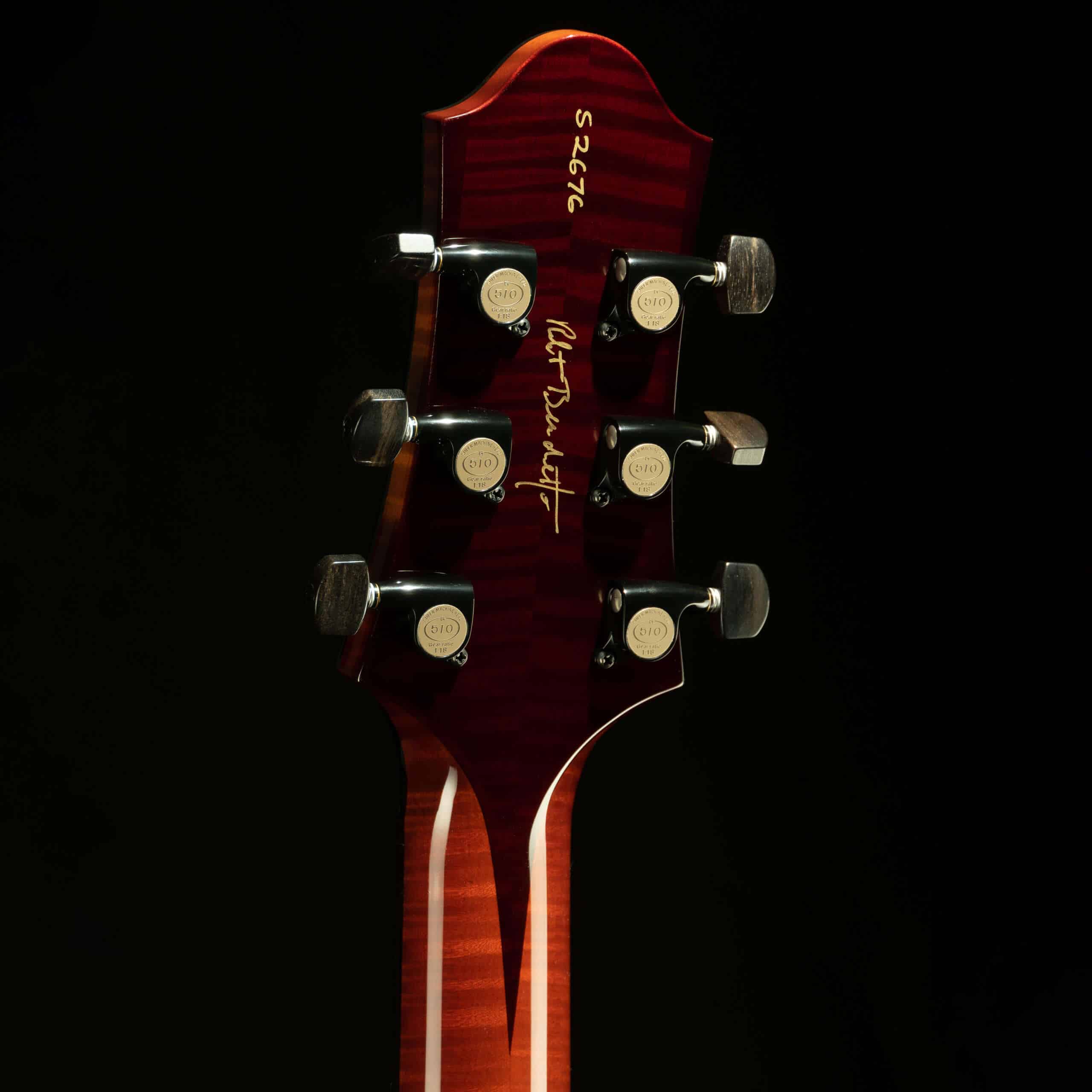 Rear view of a Benedetto Bravo Elite headstock highlighting the flamed maple veneer, the gold signature script of Robert Benedetto, the serial number, and gold Gotoh 510 tuners with ebony buttons.
