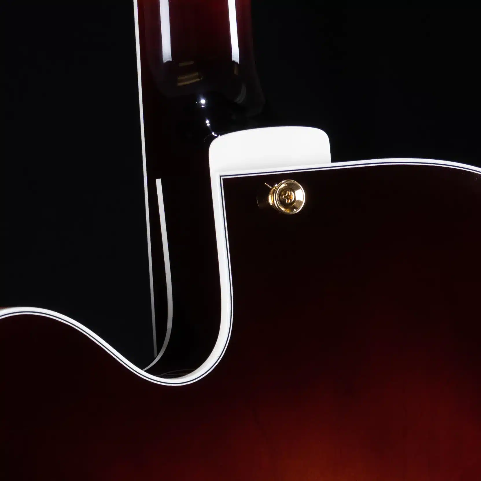 Close-up of a guitar's neck heel and upper body in a dark sunburst finish with white binding and a gold strap button.