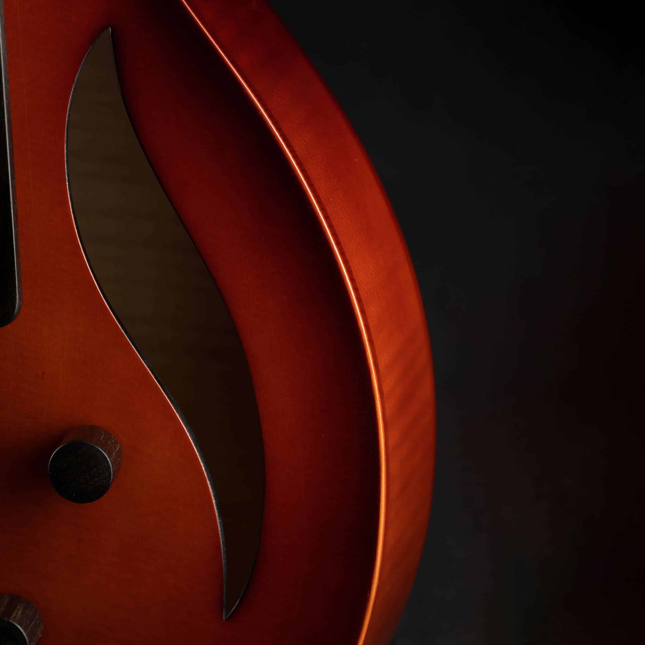 Close-up of a sunburst archtop guitar body showing a sleek, modern S-shaped sound hole.