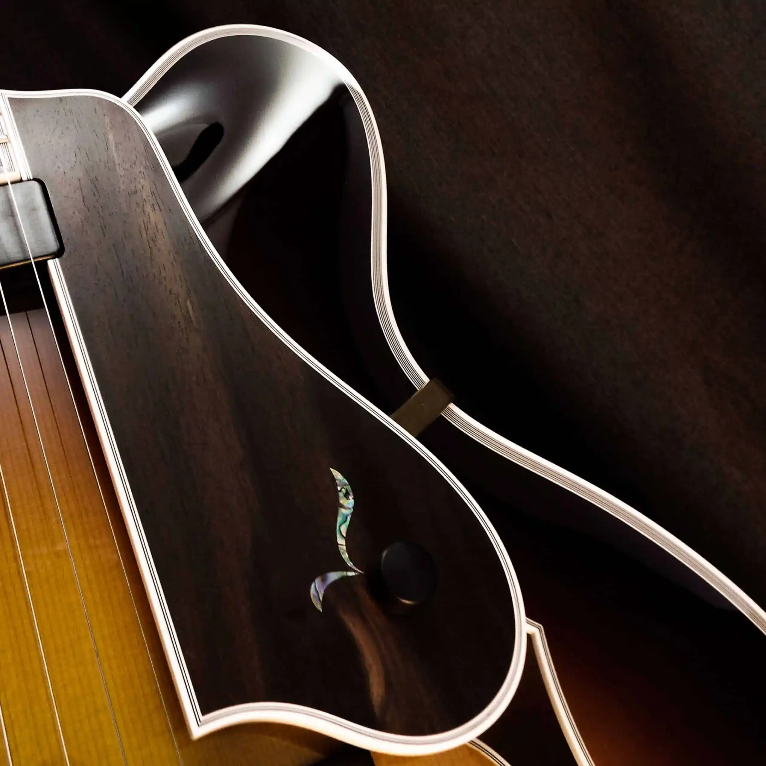 Detail of an ebony archtop pickguard with floral mother-of-pearl inlay, volume thumbwheel, and multi-ply white binding.