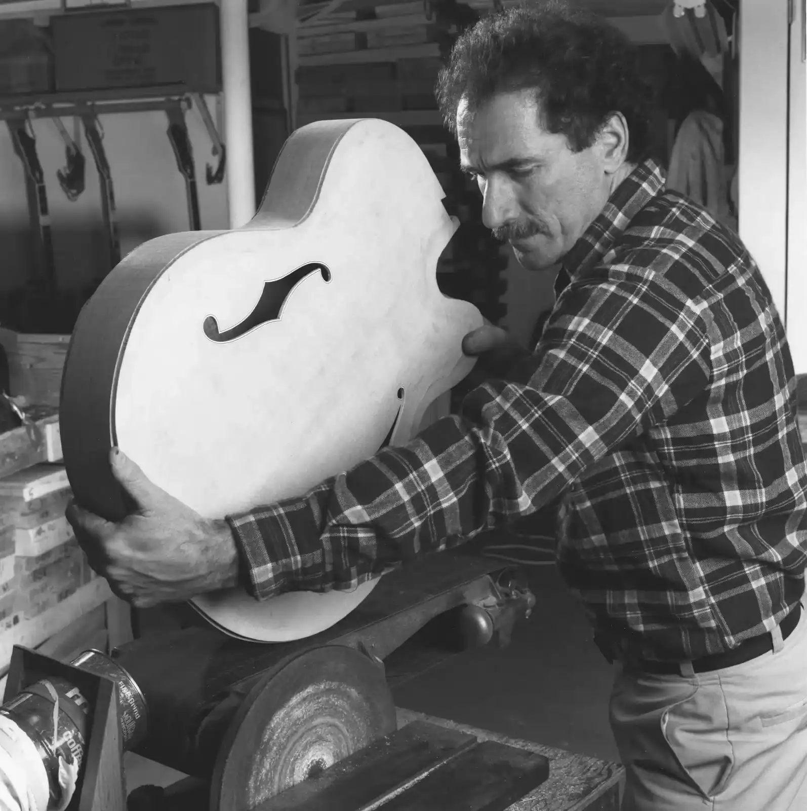 Black and white photo of luthier Bob Benedetto shaping a carved archtop guitar body in his workshop.